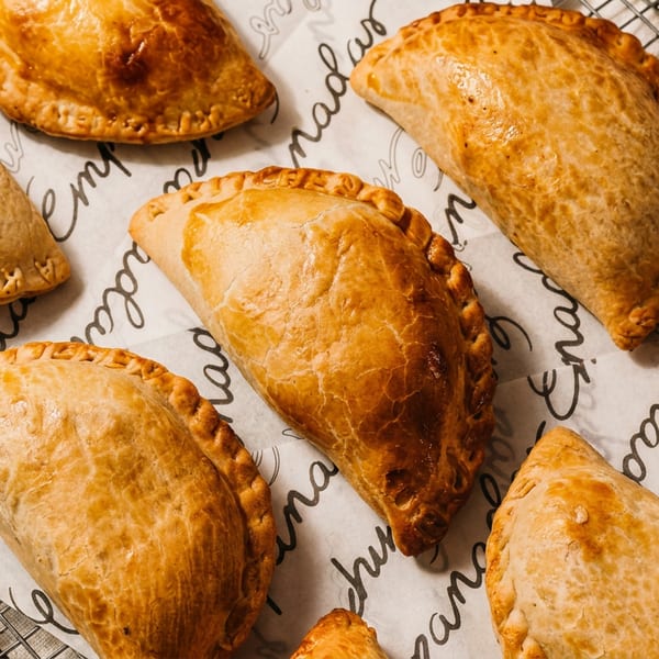 Golden-brown empanadas with crimped edges, some on a cooling rack, others on parchment paper.